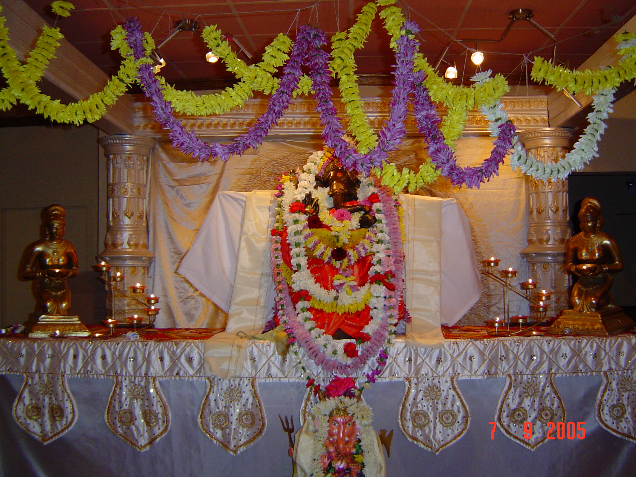 Flower-garlanded Hindu deity statue on a richly decorated indoor shrine with candles and golden statues