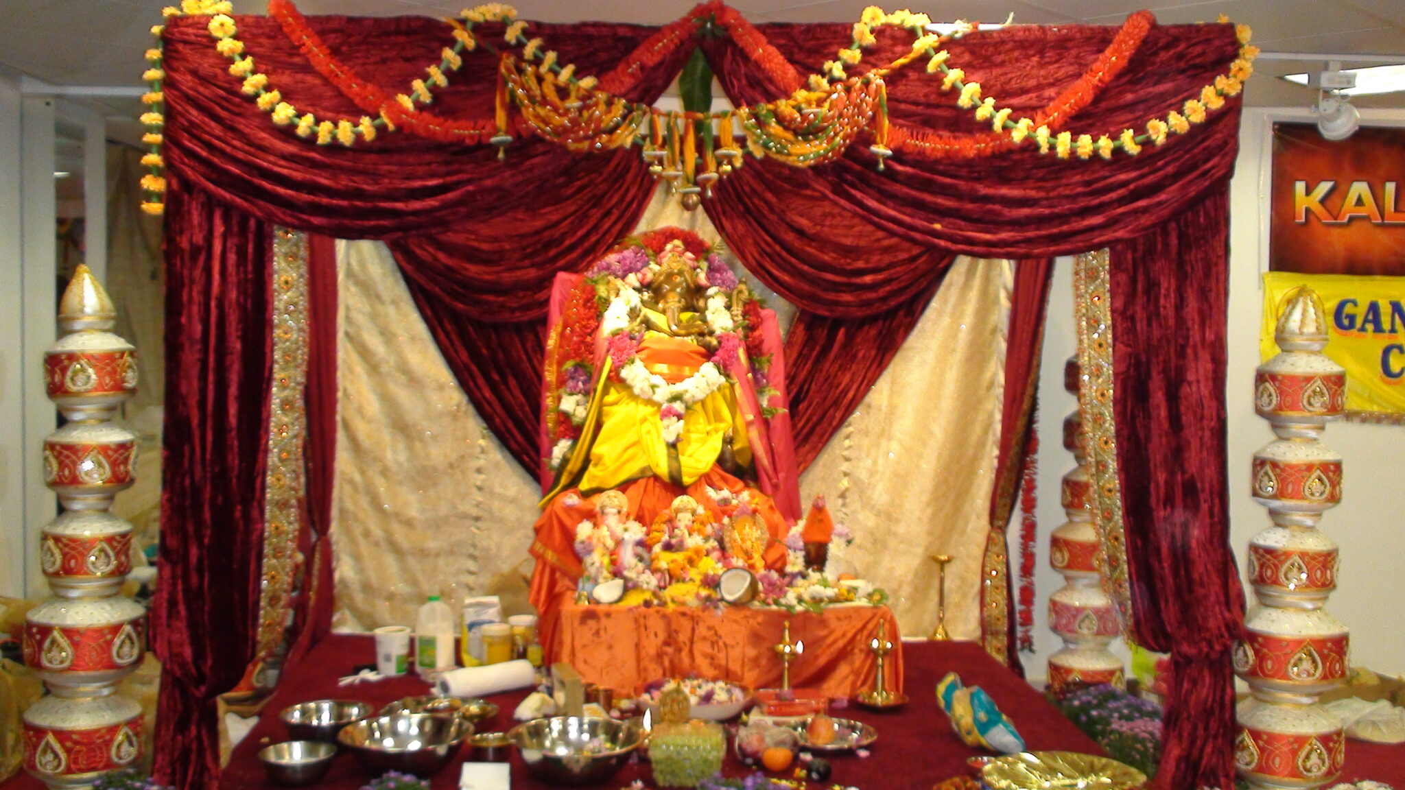 Richly decorated Hindu religious altar with flower-adorned deity statue, offerings and oil lamps